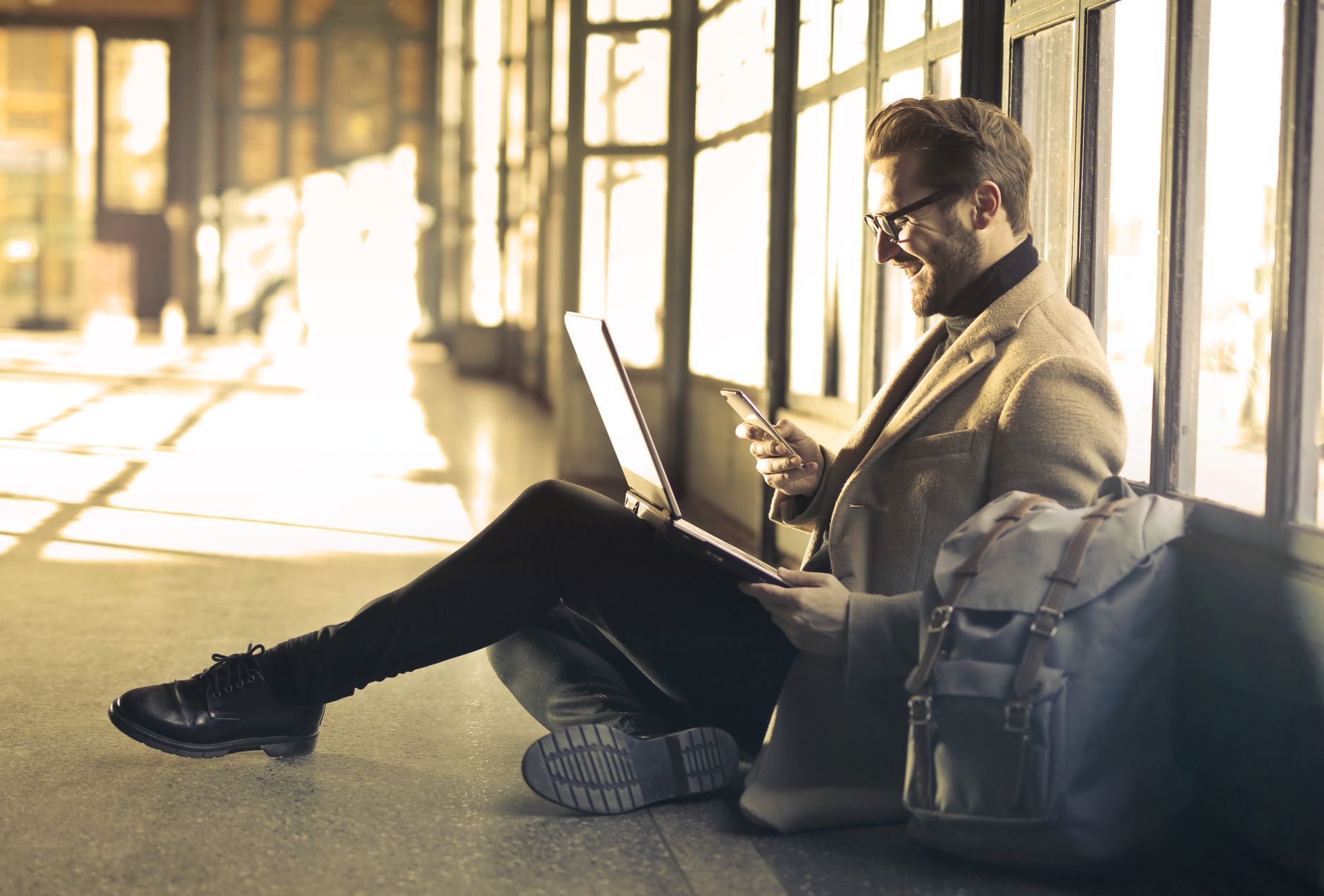 An office worker with a pleased expression transferring map data from a laptop screen to a smartphone